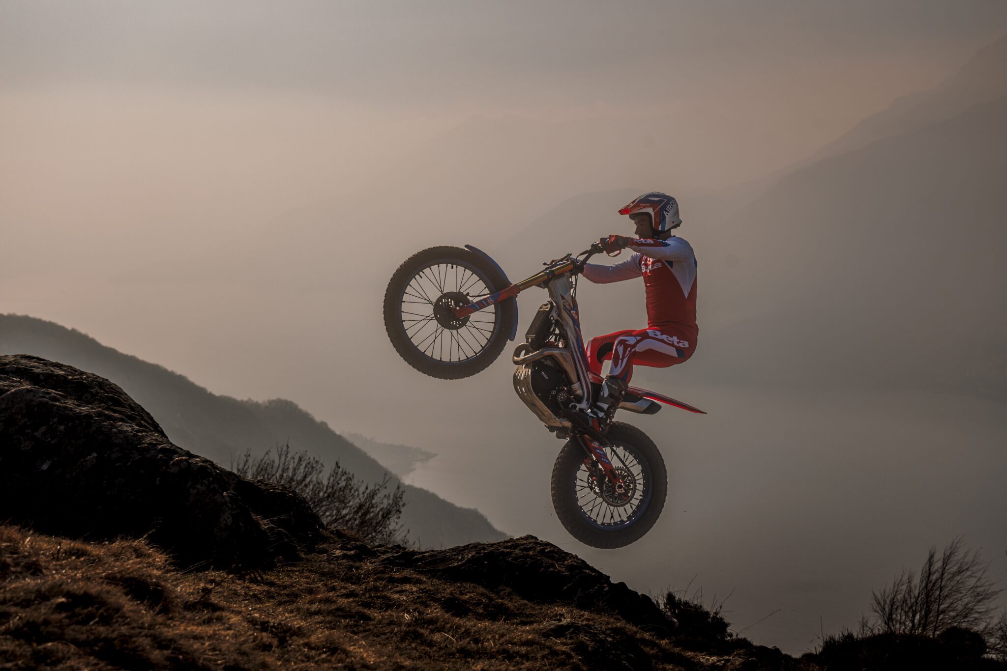 Trialfahrer macht mit einer Beta Sincro einen Wheelie in der Abenddämmerung